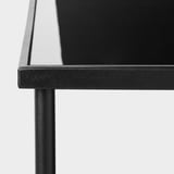 Modern, sleek glass table with black metal frame and gold accents. Tabletop reflective, sturdy metal support visible.
