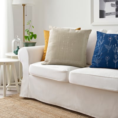 Stylish white sofa with cream, floral pillow. Blue floral and mustard cushions. Cozy decor with lamp and table items.