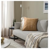 Cozy living room with light sofa, floral pillow, striped blanket, and plant.
