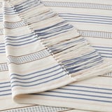 Handwoven cotton throw with intricate fringes, showcasing striped patterns in soft blue and white tones, enhanced by delicate details.
