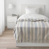 Bedroom with cream/blue striped bed, white pillow, side table lamp.