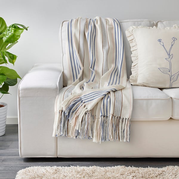 ÅKERNEJLIKA striped blanket on sofa with pillow & plant.