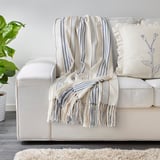 ÅKERNEJLIKA striped blanket on sofa with pillow & plant.