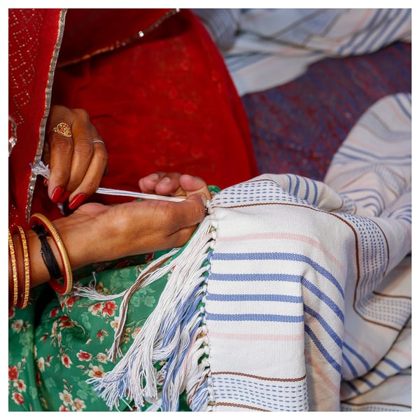 Hands weaving blue-striped cotton throw with red nails and gold bangles.