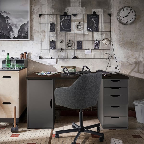 Industrial home office ALEX desk in dark grey, blending with drawers. Grey fabric chair, black wheels. Modern decor with wall art, clock.