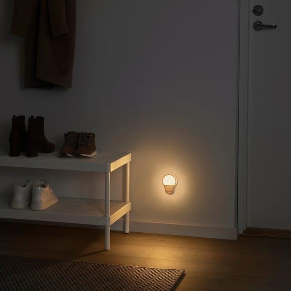 Small round glowing ANKARLÄGG light near a white shoe rack with boots and trainers. Light is on floor next to door.