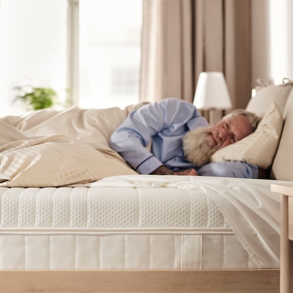 A person sleeping on an ÅNNELAND mattress, which is firm, 24 cm high, with a white cover and textured surface.