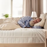 A person sleeping on an ÅNNELAND mattress, which is firm, 24 cm high, with a white cover and textured surface.