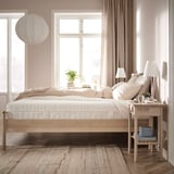 A modern bedroom with a light-colored wooden bed and beige bedding, minimalist decor, and soft lighting.