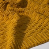 Mustard yellow knitted throw blanket with intricate textured pattern, appears soft and cozy.