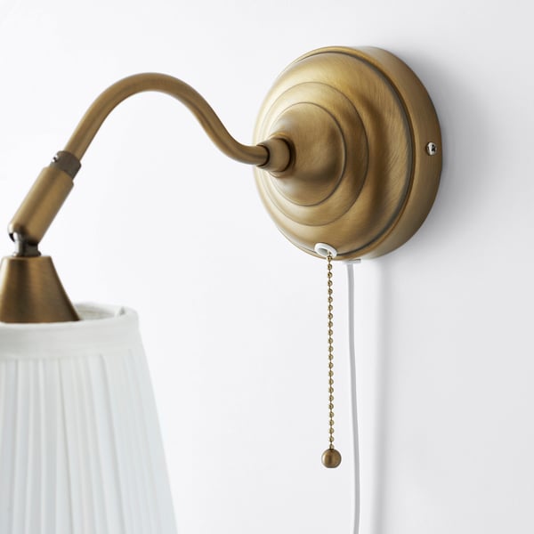 Gold wall-mounted lamp with adjustable arm and pull chain. White textured shade casts a soft light.