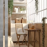 Cozy wooden outdoor table & chair set with cushion, decorated with plants in a bright corner.