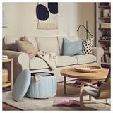 A cozy living room with a beige sofa, blue pouffe, and wooden elements.