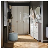 A stylish, light blue, round storage ottoman with a textured cover and wooden legs placed near an entryway.
