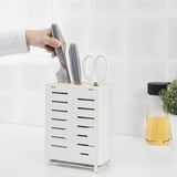Person grabbing a knife from a white AVSTEG knife holder on a counter. Nearby, theres a jar of herbs and a white scissors.