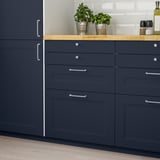 Blue AXSTAD cabinets with inset panels, wooden countertop, and silver handles. Decorated with plants and kitchen essentials.