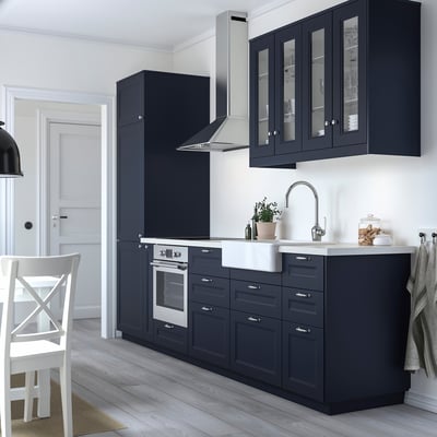 Modern kitchen with dark blue cabinets, stainless fixtures, white sink & potted plant.