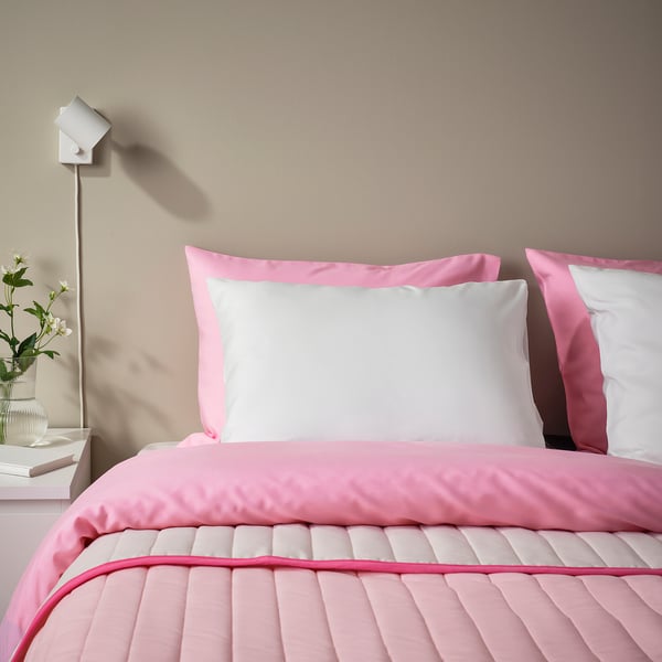 Cozy bed with pink BÄRGLIM pillow & comforter. White flowers on nightstand, minimalist light.