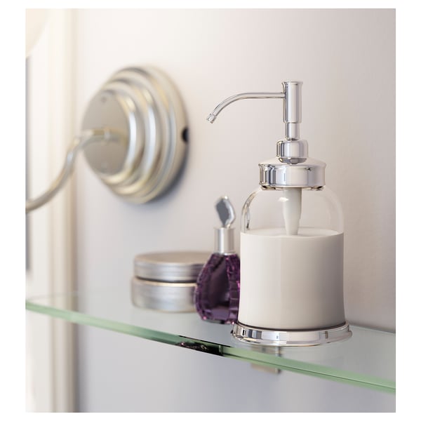 A white BALUNGEN soap dispenser on a glass shelf. It has a chrome pump and is surrounded by other small items.