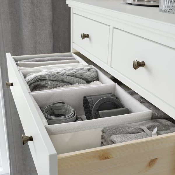 Organized white drawer with grey organizers holding knitwear, belts, and accessories, structured with fabric dividers.