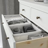 Organized white drawer with grey organizers holding knitwear, belts, and accessories, structured with fabric dividers.