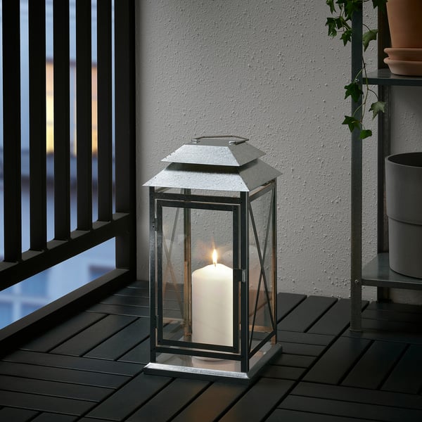 Glass lantern on wooden deck, warm light from candle inside.
