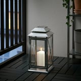 Glass lantern on wooden deck, warm light from candle inside.