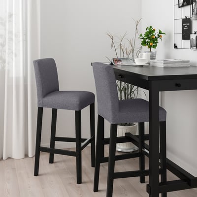 Two grey BERGMUND stools with black legs at a dark table, cushioned for comfort, taller than potted plants and cups.