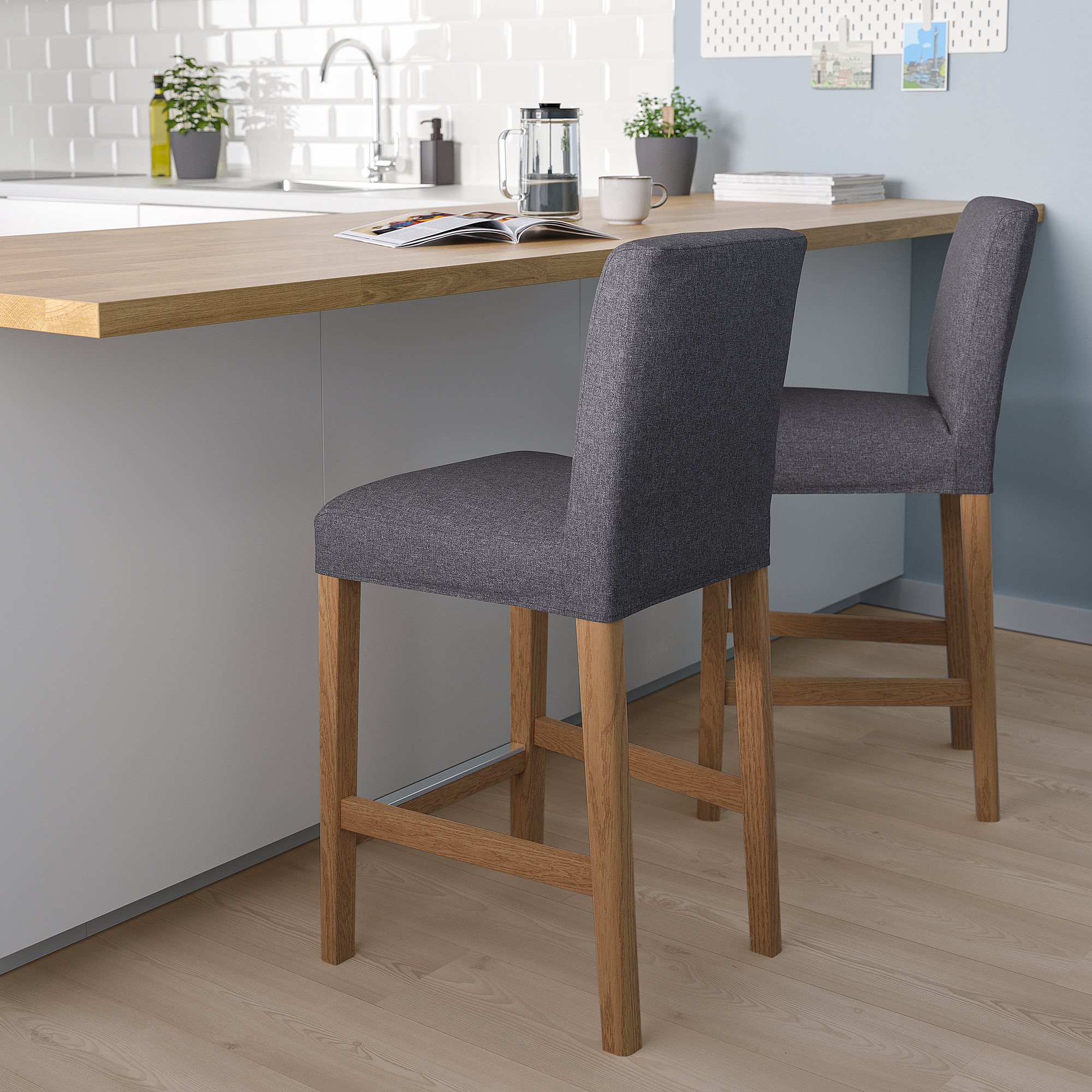 Gray BERGMUND bar stools with wooden legs at modern kitchen island, cushioned for comfort, with plants and coffee setup on countertop.