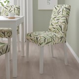 Green leafy-patterned dining chairs at white table, set against green wall and wood floor.
