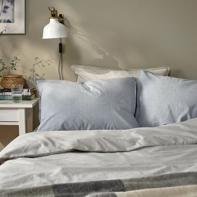 Cozy bed with blue-white striped pillows, warm lamp, side table with plant and books.