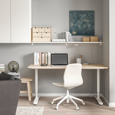 Home office setup with BERGSHULT wall shelf, white chair, wooden desk, art piece, books, and lamp. Minimalist design.