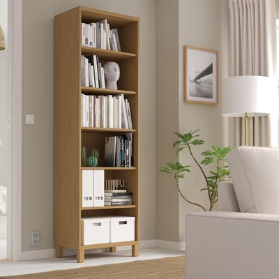 Wooden BESTÅ bookshelf in corner, filled with books and decor.