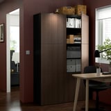 Wooden BESTÅ storage unit with adjustable shelves and soft-closing doors. It holds books, boxes, and has a modern design.