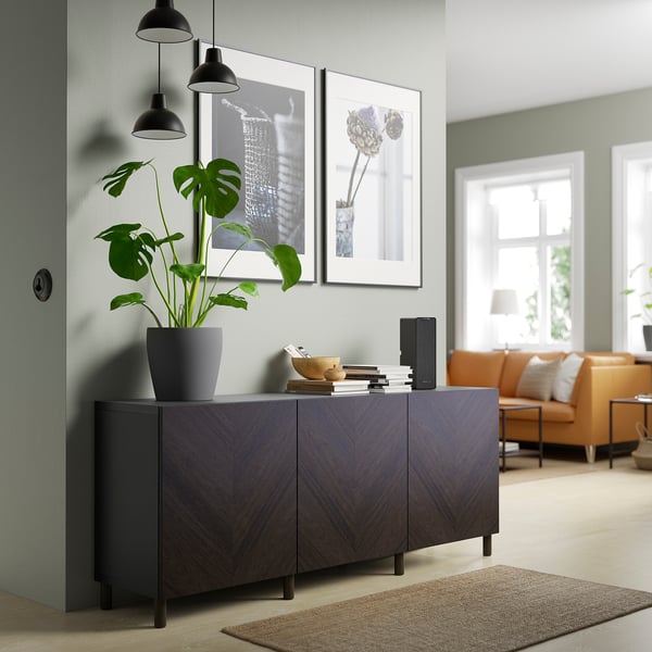 Wooden BESTÅ sideboard with plants, books, speaker. Orange sofa, rug, art.