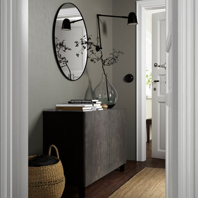 Modern entryway with BESTÅ sideboard, mirror, lights, and basket. Books and vase on sideboard, wooden floors, jute rug.