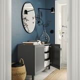 Modern hallway with black BESTÅ cabinet, blue wall, round mirror, and woven basket.