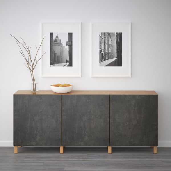 Gray sideboard with wooden top, two black & white framed photos, bowl of oranges, and vase.
