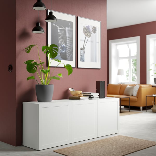 Modern living room with BESTÅ, plant, books, speaker, framed pics, orange sofa, large window, rug.