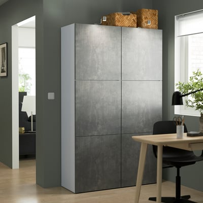 Gray BESTÅ shelving with textured doors, taller than desk & chair, blue-green wall.