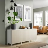 Modern living room with BESTÅ sideboard, plants, books, pendant lamps, orange couch, and beige rug.