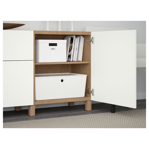 White cabinet with open door revealing boxes and books on shelf, white drawer below.