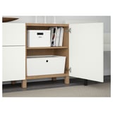 White cabinet with open door revealing boxes and books on shelf, white drawer below.
