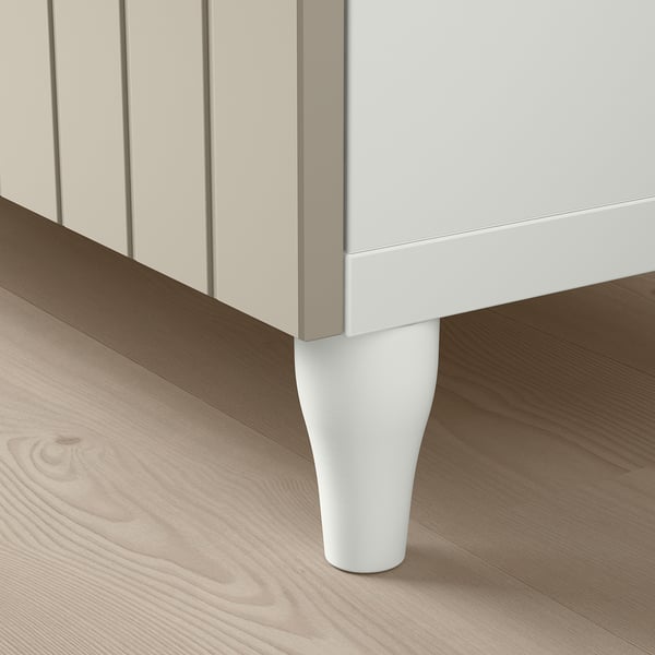 White cabinet with slim legs on wooden floor. Clean, modern design.