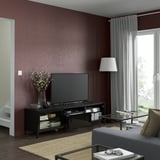 Modern living room: maroon walls, BESTÅ tv bench, books, flowers, remote on glass table in front of gray sofa.