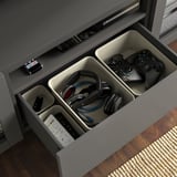 Open BESTÅ tv bench showing organized cables, controllers, headphones, and remotes in compartments. Gray with soft-close drawers.