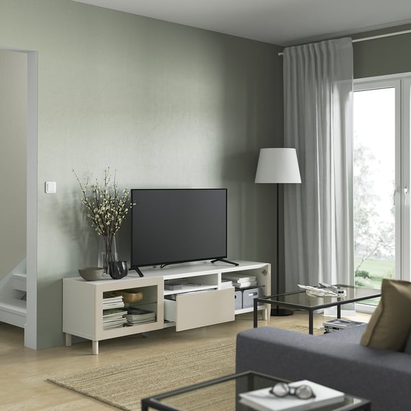 Modern living room with BESTÅ tv bench, white with shelves and drawers, flat-screen tv, floor lamp, glass coffee table, gray sofa.