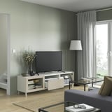 Modern living room with BESTÅ tv bench, white with shelves and drawers, flat-screen tv, floor lamp, glass coffee table, gray sofa.