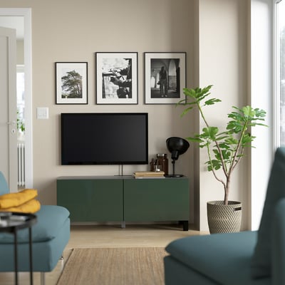 Modern living room with BESTÅ green tv stand, adjustable shelves, and wall photos. A tall green plant complements a teal armchair.