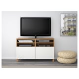 Modern tv stand with wooden top, white drawers, flat-screen tv, and storage ottomans.
